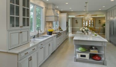white and gray cabinetry with white tops and light flooring includes warmth from gold tone faucets, cabinet pulls and light fixtures