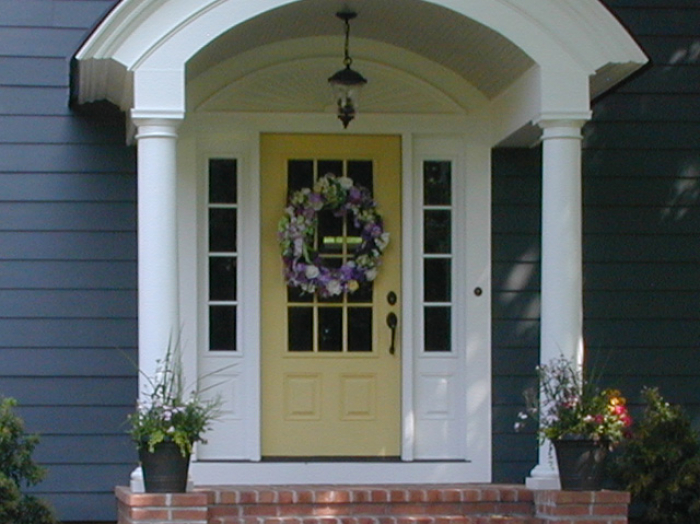 Front-entry barrel shaped porch roof over yellow door with side lights
