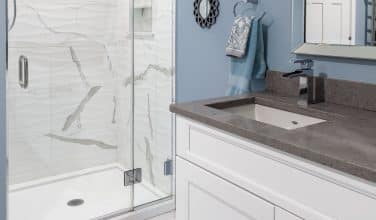 basement bath remodel with walk in marble shower and white shaker cabinetry with dark gray stone top